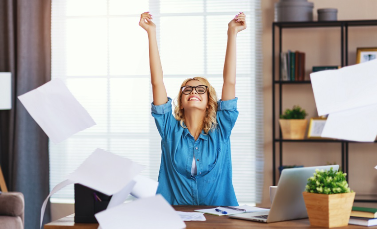 Woman at desk, arms raised in victory