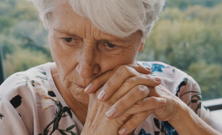 Close-up on face of elderly woman looking worried, her hands crossed just beneath her mouth
