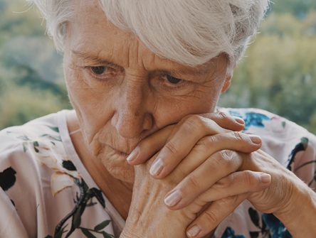 Close-up on face of elderly woman looking worried, her hands crossed just beneath her mouth