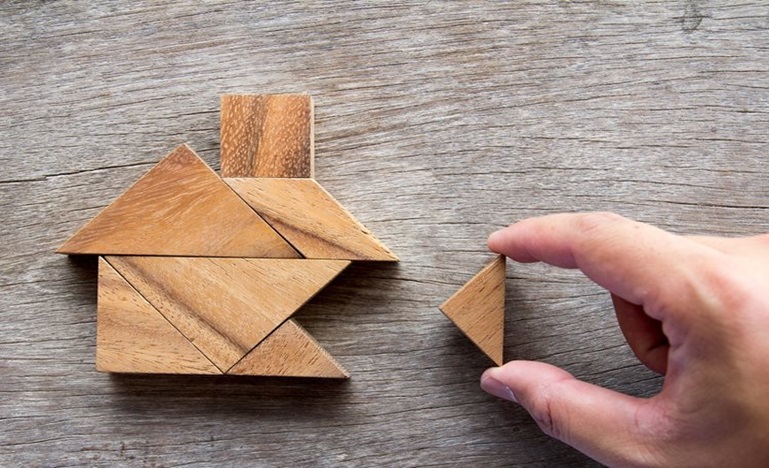 A wooden puzzle forms a house, a hand puts in the last piece