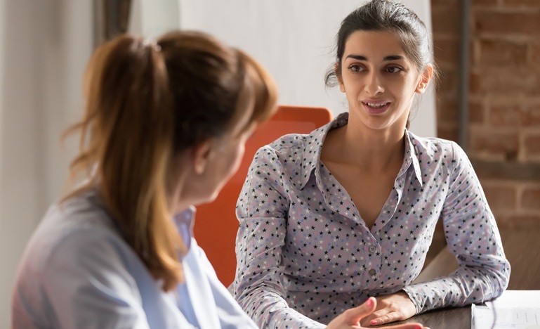 A Young female lawyers sits at a table listening, with an expression of understanding, to the female client seated next to her.