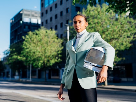 women in a business suit standing in front of an office building on a city street, carry an astronaut's helmet under one arm
