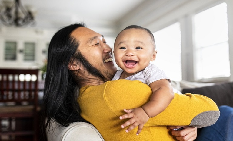 A young man lifts up baby in his arms as they both smile