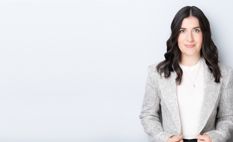 Photo of Katy Commisso, dressed in white shirt and grey jacket, against a light grey background