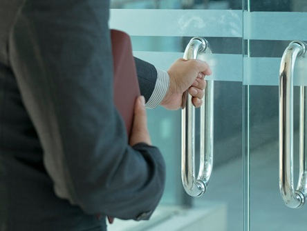 arm and hand of woman in business suit, holding dayplanner and opening glass office door