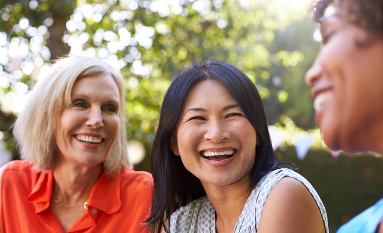 Three middle-aged women sitting outside talking and laughing