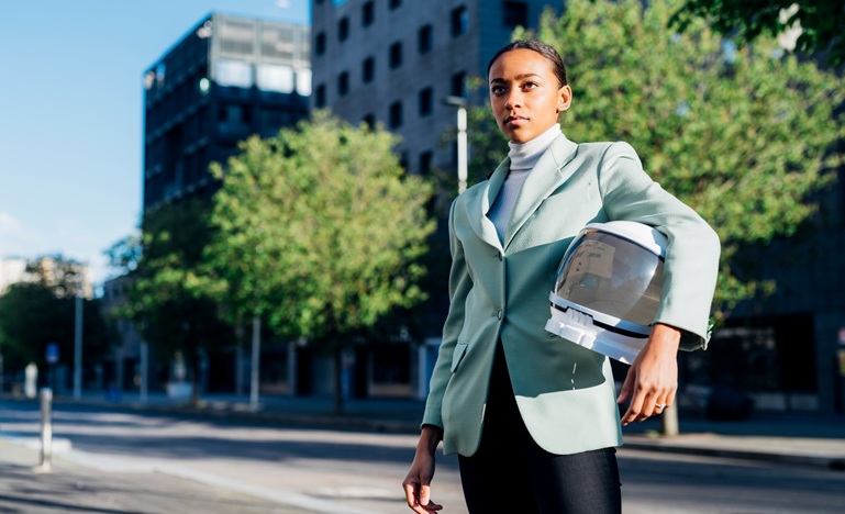 women in a business suit standing in front of an office building on a city street, carry an astronaut's helmet under one arm