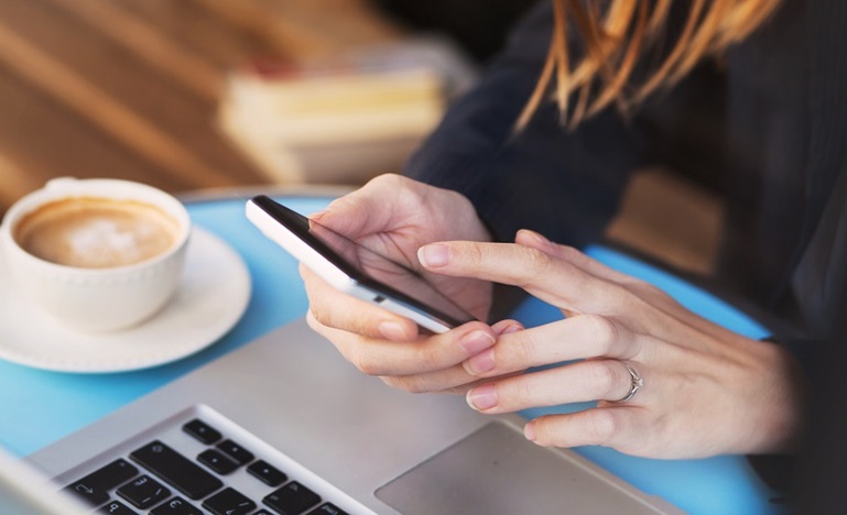 Close-up of the hands of a woman at a cafe as she scrolls through news on her phone