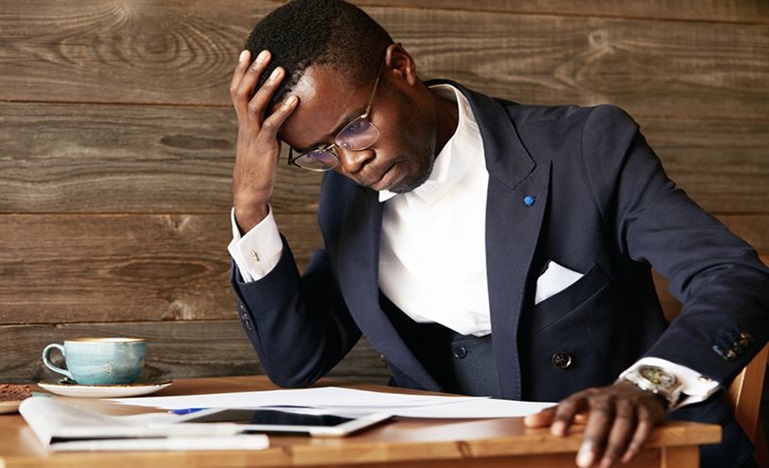 Man holding his head while looking at some documents on table