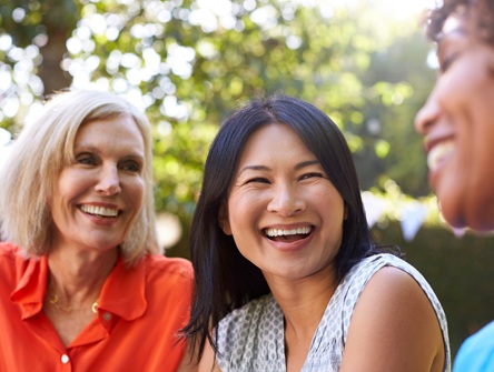 Three middle-aged women sitting outside talking and laughing